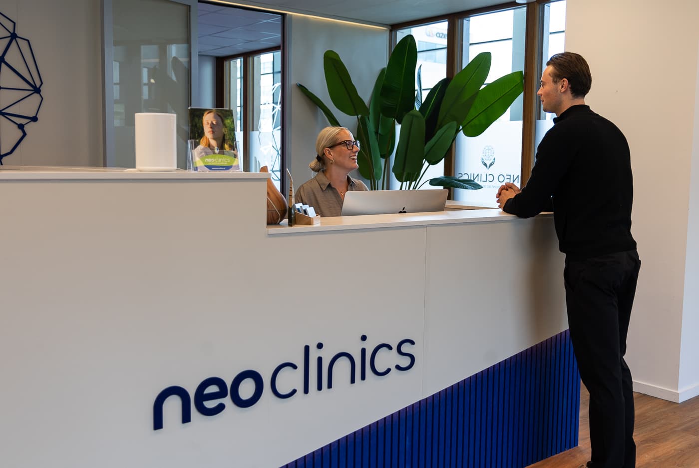 De ontvangstbalie van Neo Clinics, waar een cliënt wordt verwelkomd